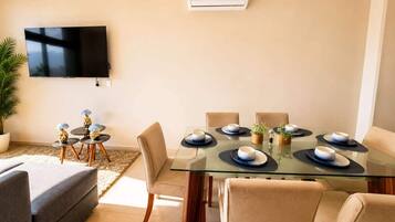 A modern living room with a glass dining table set for six, surrounded by beige sofas and chairs.