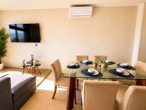 A modern living room with a glass dining table set for six, surrounded by beige sofas and chairs. - Arena Vive El Parque Apartamentos  (Monterrey)