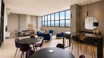 A modern conference room with a large table, multiple chairs, a bar area, and a large window offering a city view.