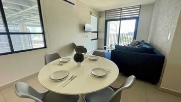 Un espacio habitable moderno con una mesa de comedor dispuesta para cuatro personas, un sofá y un televisor montado en la pared.