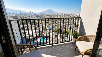 A balcony with a city view, a pool, and wicker furniture.