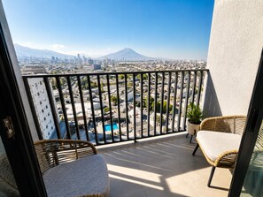 A balcony with a city view, a pool, and wicker furniture. - Arena Vive El Parque Apartamentos  (Monterrey)