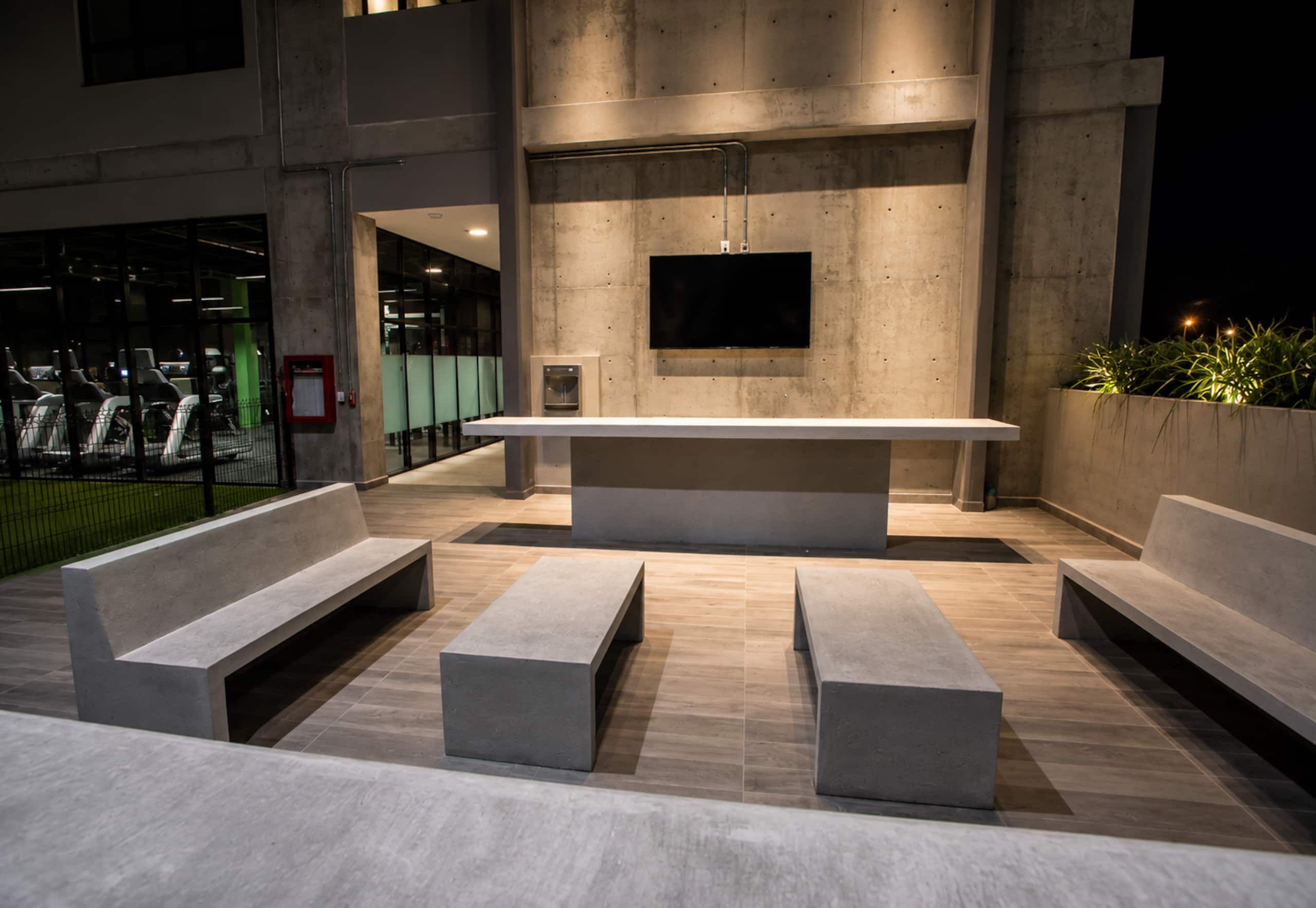 An outdoor seating area with benches and a flat table, a mounted television, and a water dispenser.