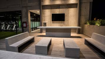 An outdoor seating area with benches and a flat table, a mounted television, and a water dispenser.