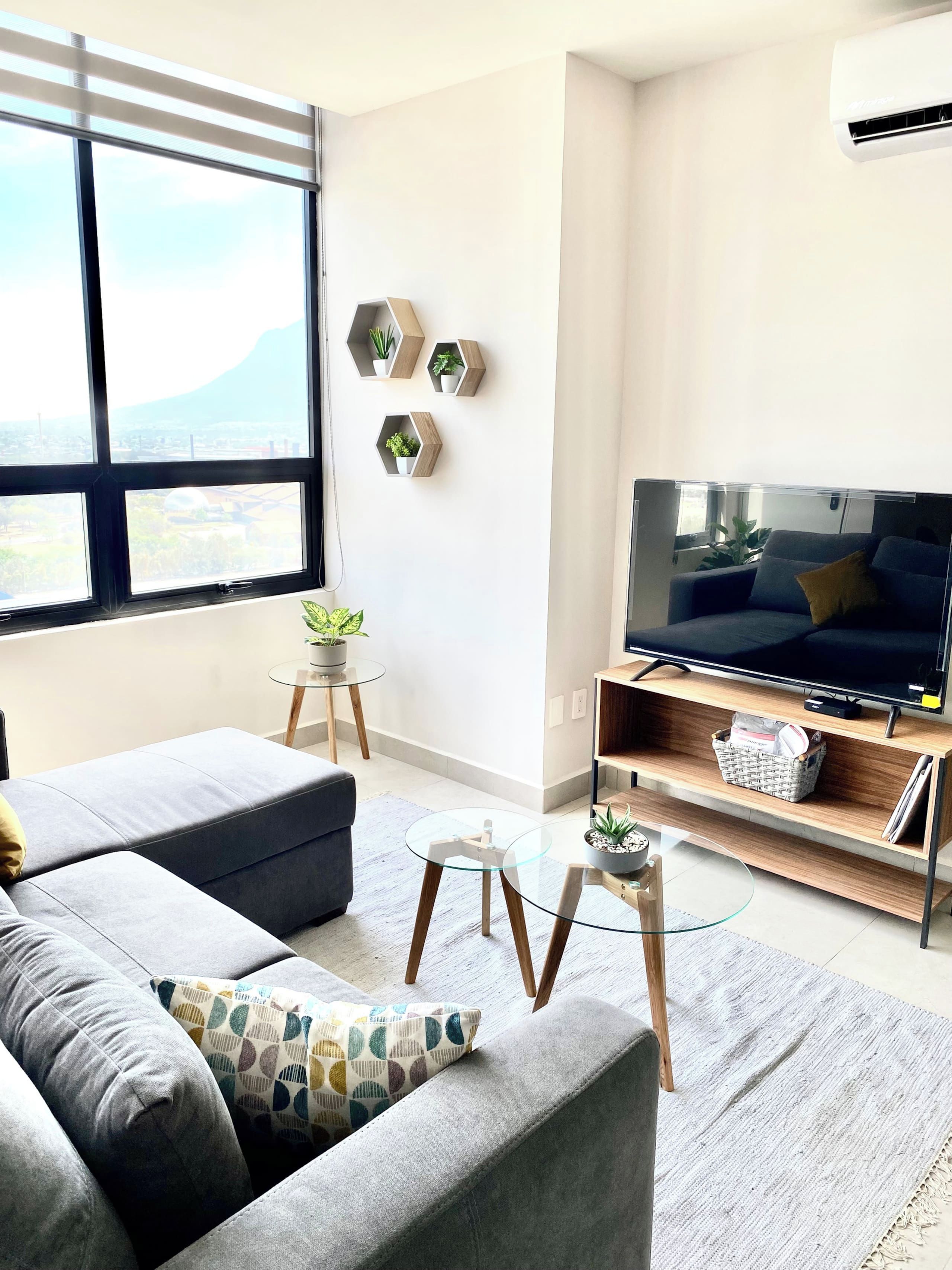Un salon moderne avec un canapé, une table basse en verre, un téléviseur posé sur un meuble en bois et une vue sur une montagne, visible à travers de grandes fenêtres.
