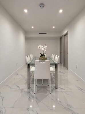 Une salle de conférence moderne avec une table en verre, des chaises blanches, un vase de fleurs blanches et un luminaire au plafond.
