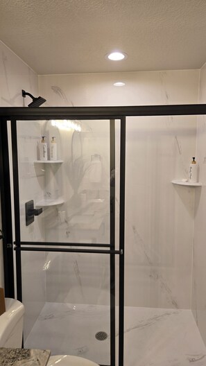 Ein modernes Badezimmer mit einer Duschkabine aus Glas, weißen Marmorwänden und einer sichtbaren Toilette.