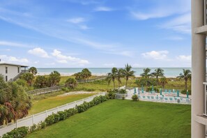 Een resort met uitzicht op het strand, een zwembadgedeelte met ligbedden en een witte hekken.