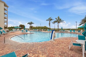 A pool area with lounge chairs and umbrellas, surrounded by palm trees and a clear sky. - Elevated Beach Escape on Treasure Island (Treasure Island)