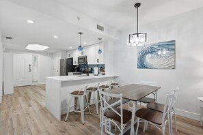 A modern kitchen with white cabinetry, a central island, and bar stools. - Elevated Beach Escape on Treasure Island (Treasure Island)