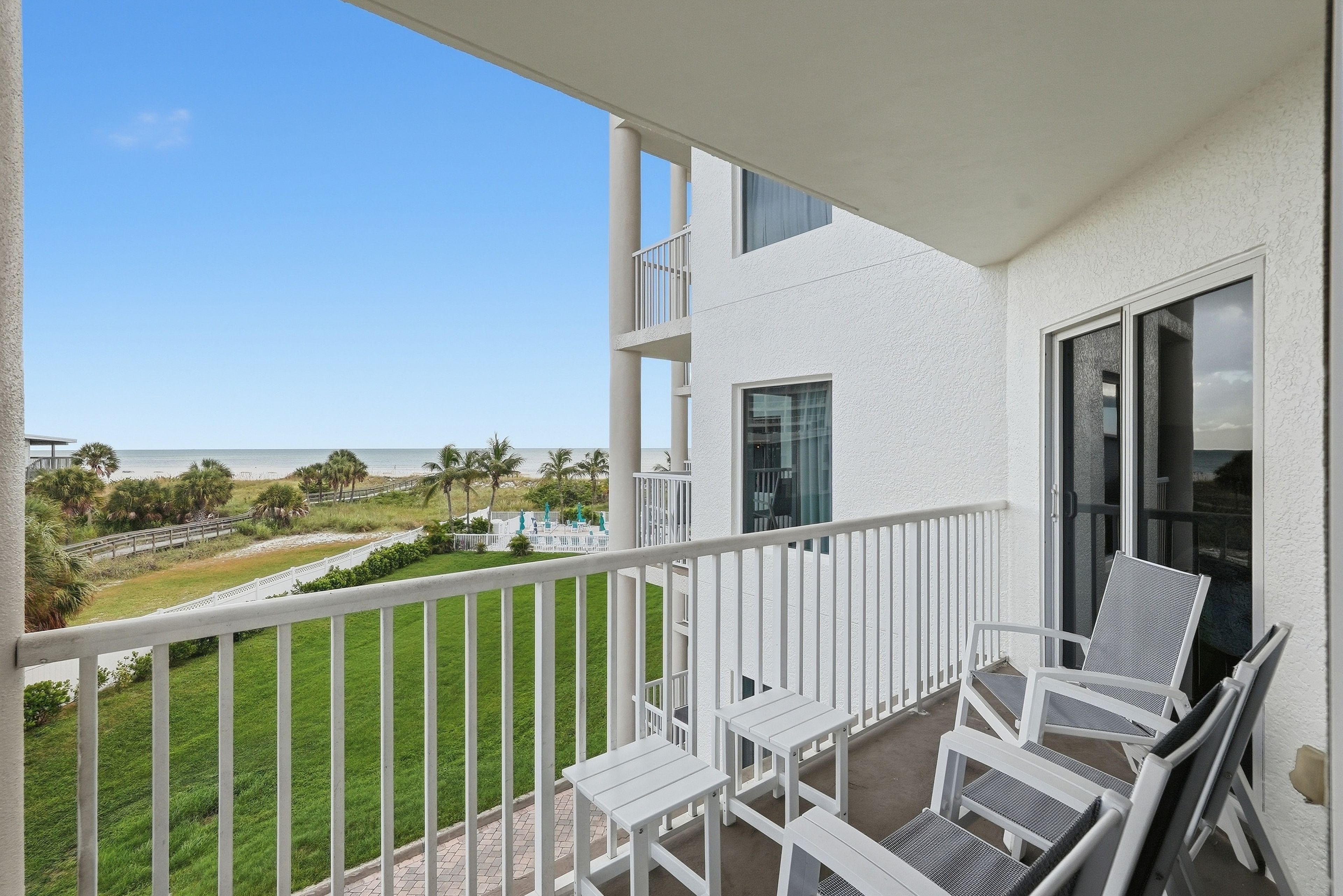 A balcony with white railings, a view of the beach, and outdoor furniture.