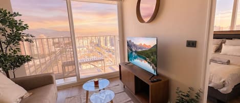 A modern living room with a balcony, a flat-screen TV, a sofa, a coffee table, and a bed.