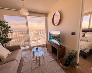Ein modernes Wohnzimmer mit Balkon, einem Flachbildfernseher, einer Couch, einem Couchtisch und einem Bett.