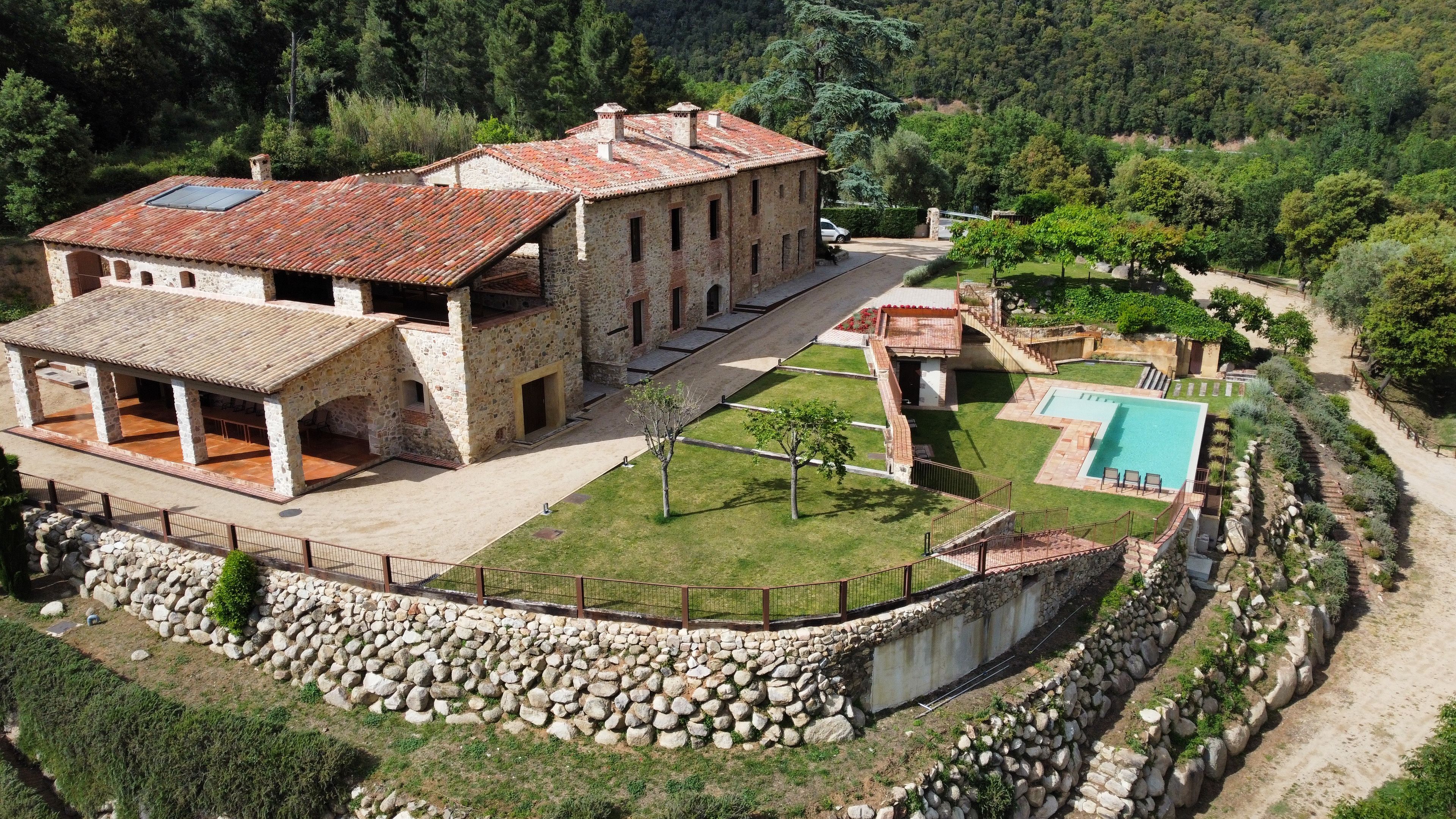 A stone building with a swimming pool, surrounded by a stone wall and a garden.