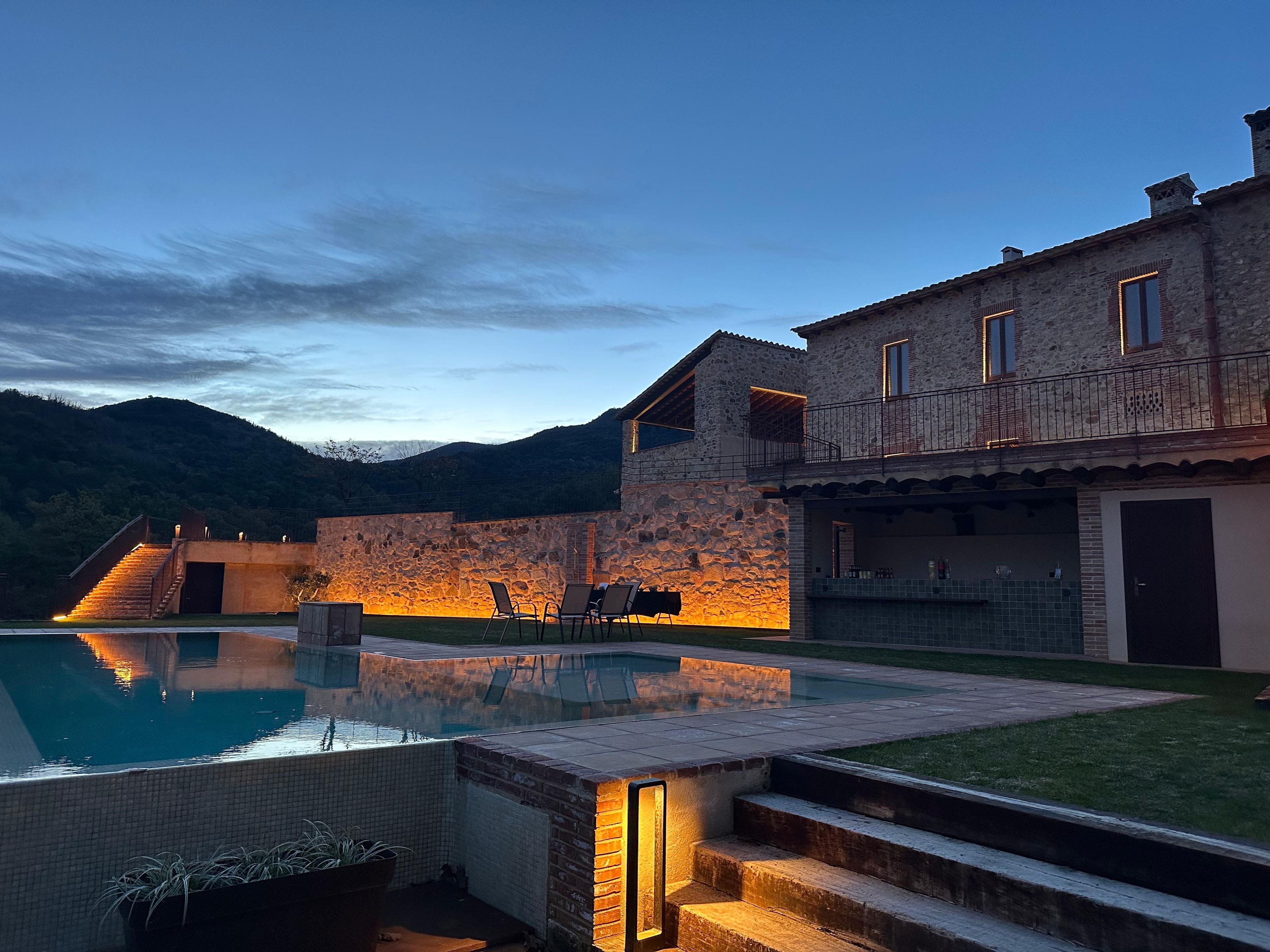 A stone building with a pool, outdoor seating, and a staircase leading to a balcony.