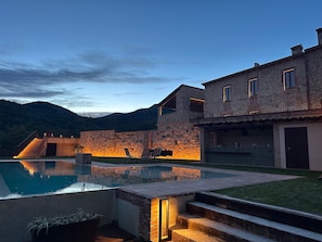 A stone building with a pool, outdoor seating, and a staircase leading to a balcony.
