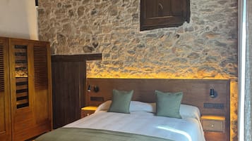 A bedroom with a stone wall, wooden headboard, a bed with green bedding, a nightstand, and a wooden chest of drawers.