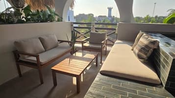 Terraço no telhado com telhado de palha, um sofá, uma mesa de madeira e vista para uma torre ao longe.