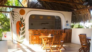 Un restaurant doté d’un toit de chaume, de meubles en bois et offrant une vue sur la verdure.