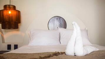 Un lit avec des oreillers blancs et une couverture, un miroir rond accroché au mur et un luminaire suspendu.