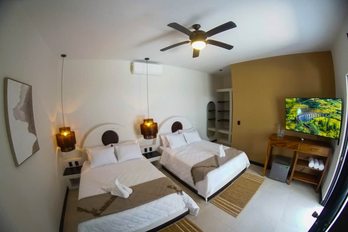 Ein Hotelzimmer mit zwei Betten, einem Deckenventilator, einem Fernseher und einem kleinen Schreibtisch mit Ablagefläche.