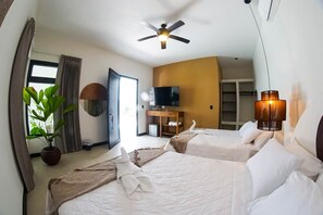 Quarto de hotel com duas camas, ventilador de teto, televisão, planta e abajur.