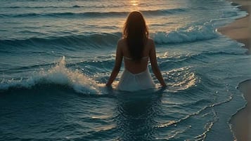 Iemand staat in ondiep water aan een strand tijdens de zonsondergang.