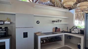 Una cocina compacta con techo de paja, refrigerador integrado, microondas y pileta.