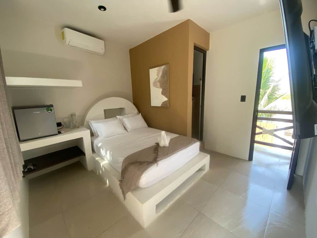 Ein modernes Schlafzimmer mit Bett, Schreibtisch und einer Tür, die auf einen Balkon führt.