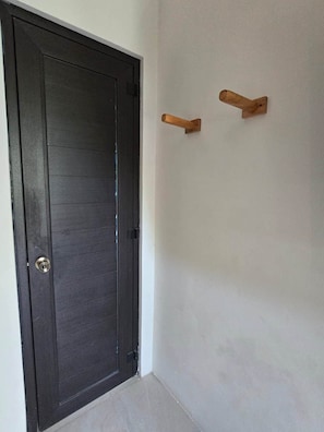 A dark wooden door with a silver handle, a white wall, and two wooden hooks mounted on the wall.