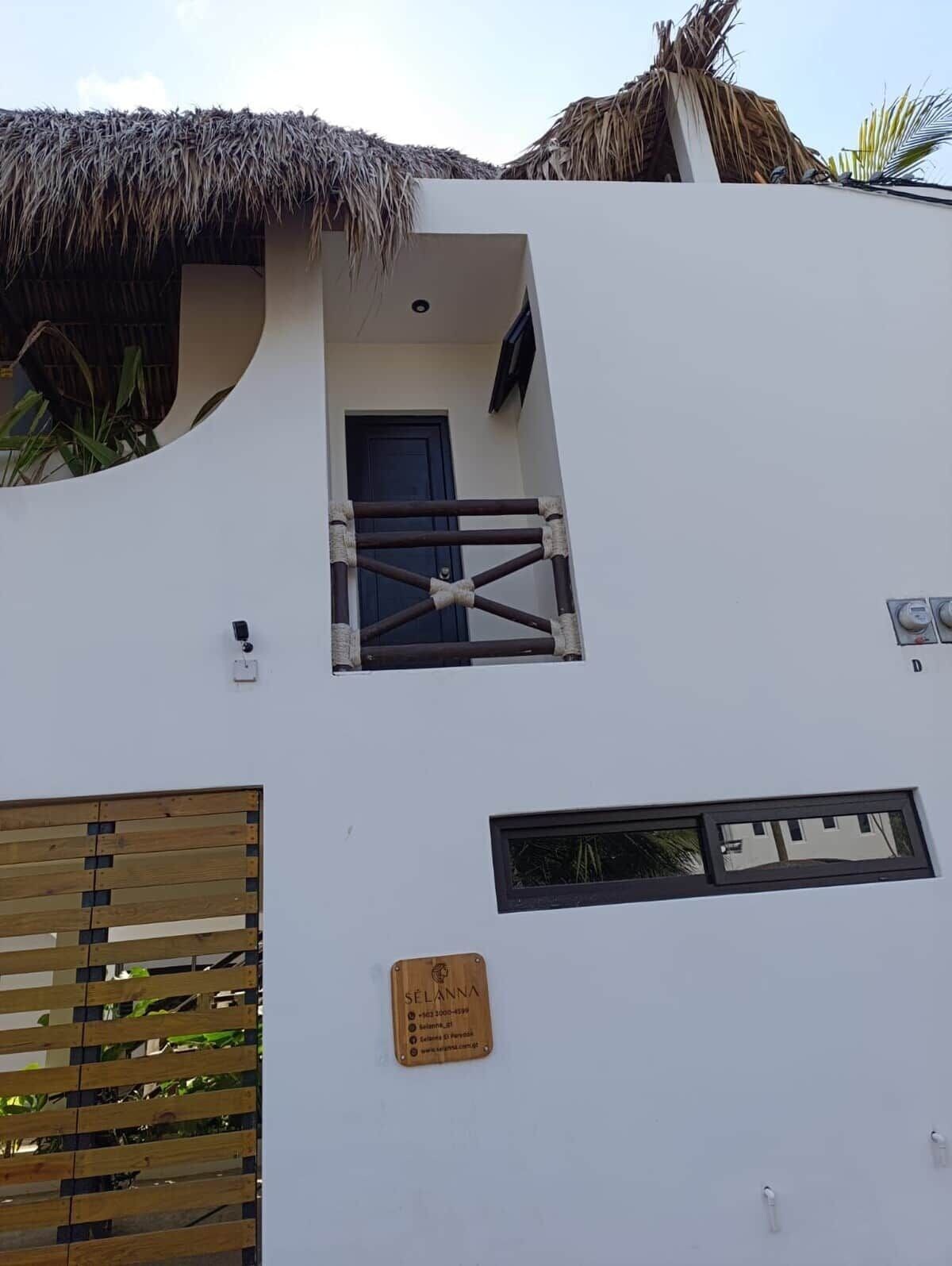 A building with a thatched roof, a small balcony with a metal railing, and a wooden panel on the wall.
