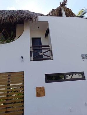 A building with a thatched roof, a small balcony with a metal railing, and a wooden panel on the wall.