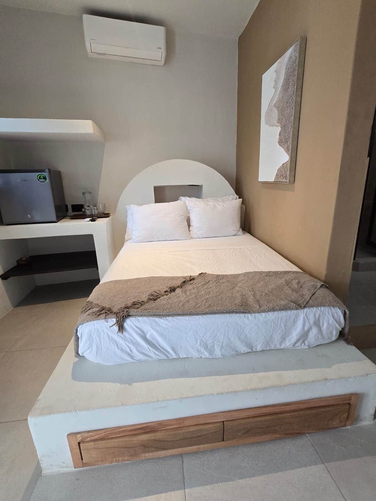 A bed with a headboard, a bedside table, a laptop, and a wall-mounted air conditioner.