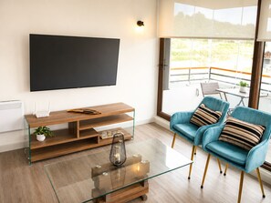Een moderne woonkamer met een flatscreen televisie, een houten tv-meubel, een glazen salontafel en blauwe fauteuils.