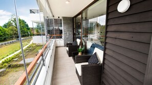 Ein Balkon mit Korbmöbeln und Glasgeländer mit Blick auf eine angelegte Grünfläche.