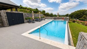 Ein rechteckiger Swimmingpool mit Metallleiter, umgeben von einer Steinmauer und einer gepflasterten Liegefläche.