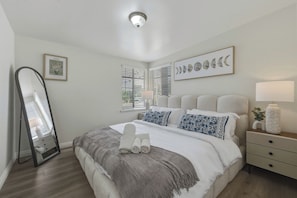 Un dormitorio con cama, mesita de noche, espejo y ventana con persianas.