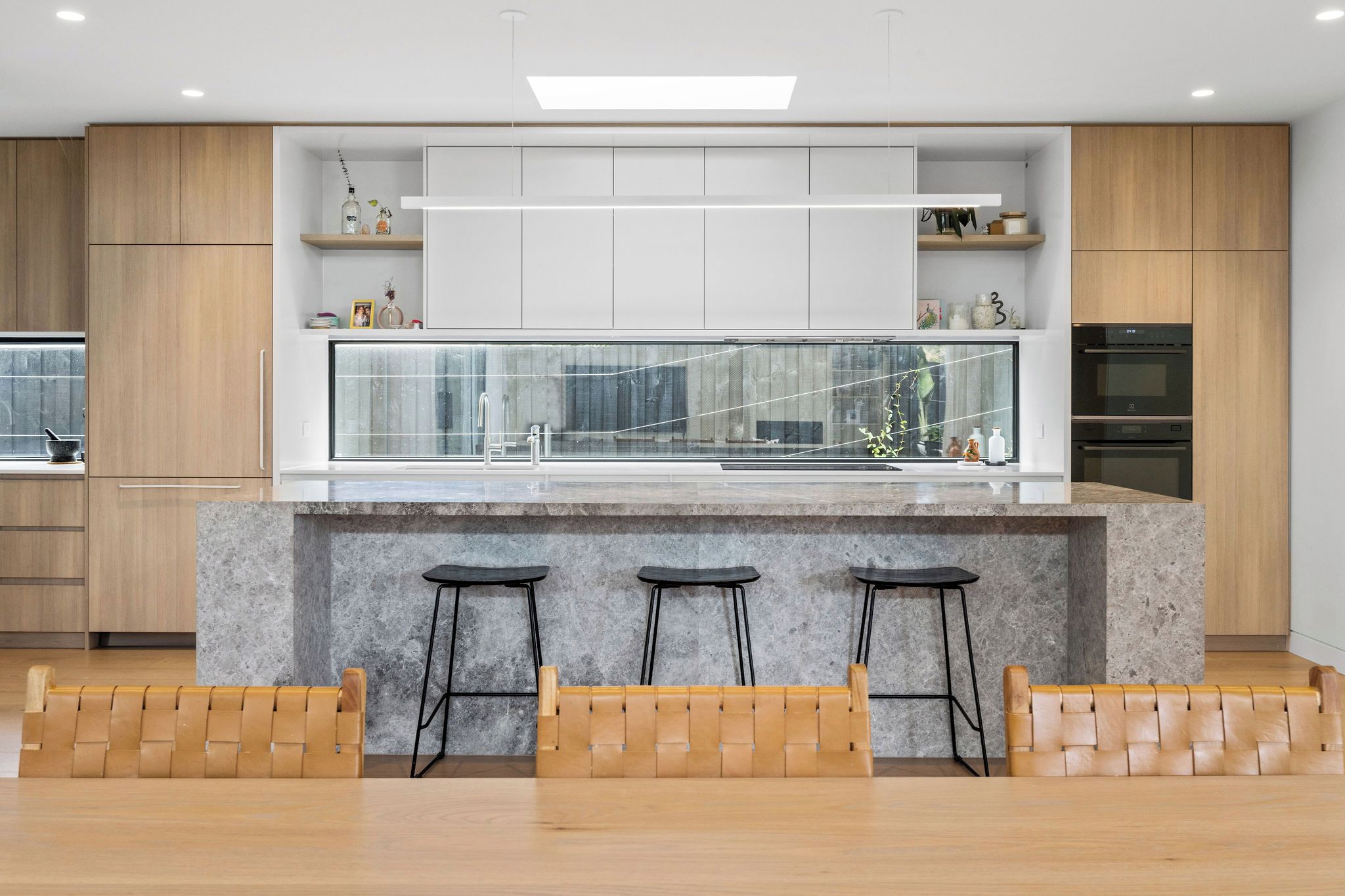 A modern kitchen with a marble island, bar stools, wooden cabinets, and built-in appliances.
