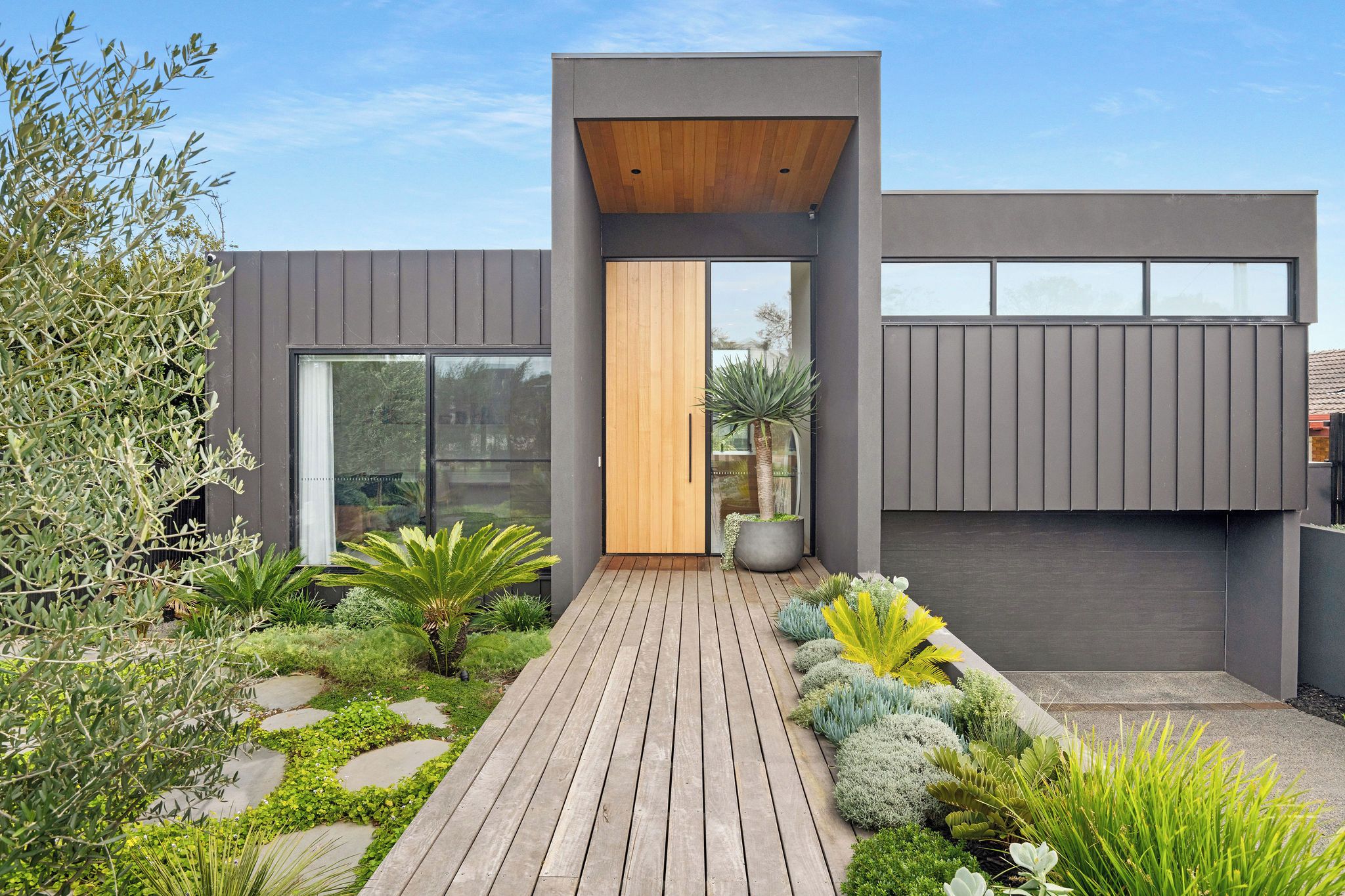 A modern house with a wooden deck, large windows, and a variety of plants.