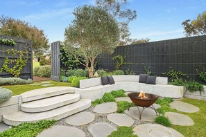 A modern outdoor patio with a curved seating area, a fire pit, and a stone pathway. - Sanctuary 30. Luxury beach escape (Blairgowrie)