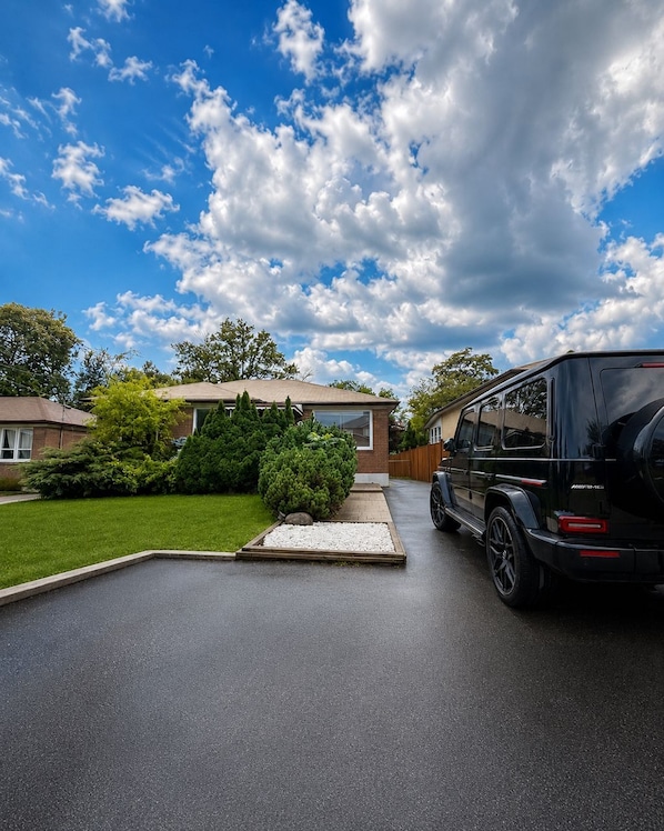 A residential driveway with a black SUV parked on the right, a well-maintained lawn, and a house with a visible garage door.