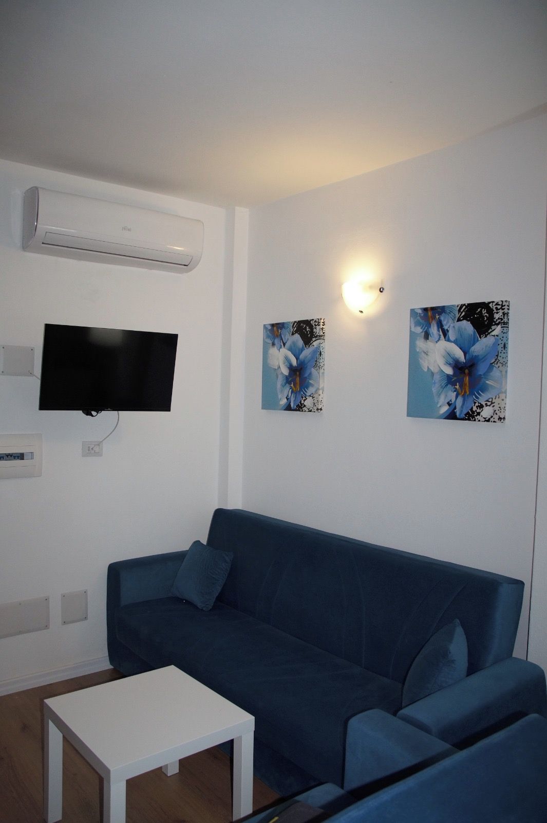 Ein Wohnzimmer mit einem blauen Sofa, einem weißen Couchtisch, einem Flachbildfernseher und zwei Wandleuchten.