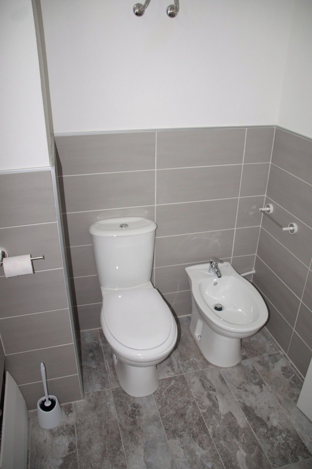 Ein Badezimmer mit Toilette, Bidet und Toilettenpapierhalterung.