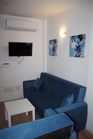 Ein Wohnzimmer mit einem blauen Sofa, einem flachbildfernseher an der Wand und zwei Wandleuchten.