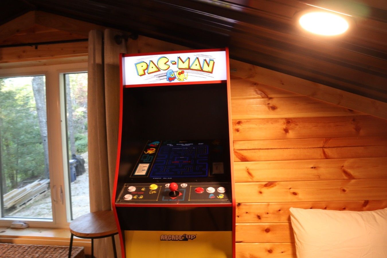 A Pac-Man arcade machine in a cabin with wooden walls and a window.