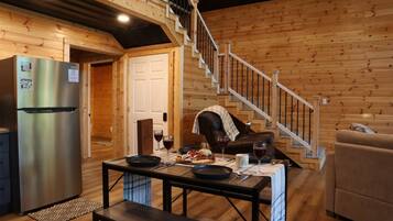 A wooden cabin interior with a dining table set for two, a refrigerator, and a staircase.