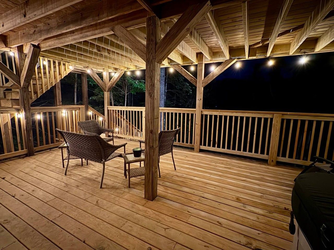 A wooden deck with a table and chairs, surrounded by railings and string lights.