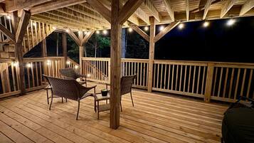 A wooden deck with a table and chairs, surrounded by railings and string lights.