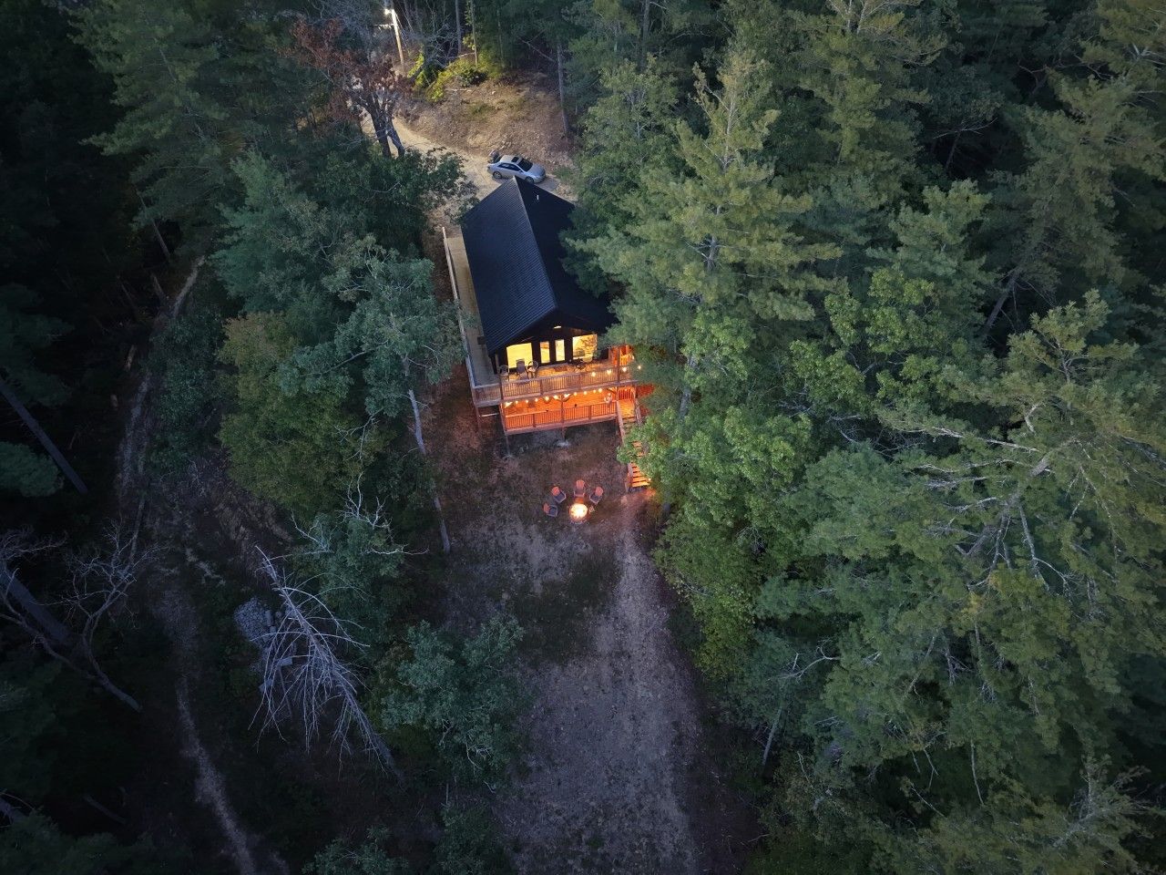 A cabin surrounded by dense forest, accessible by a dirt path.