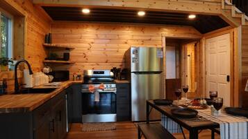 A compact kitchen with wooden walls, a stainless steel refrigerator, and a dining area with a table set for two.